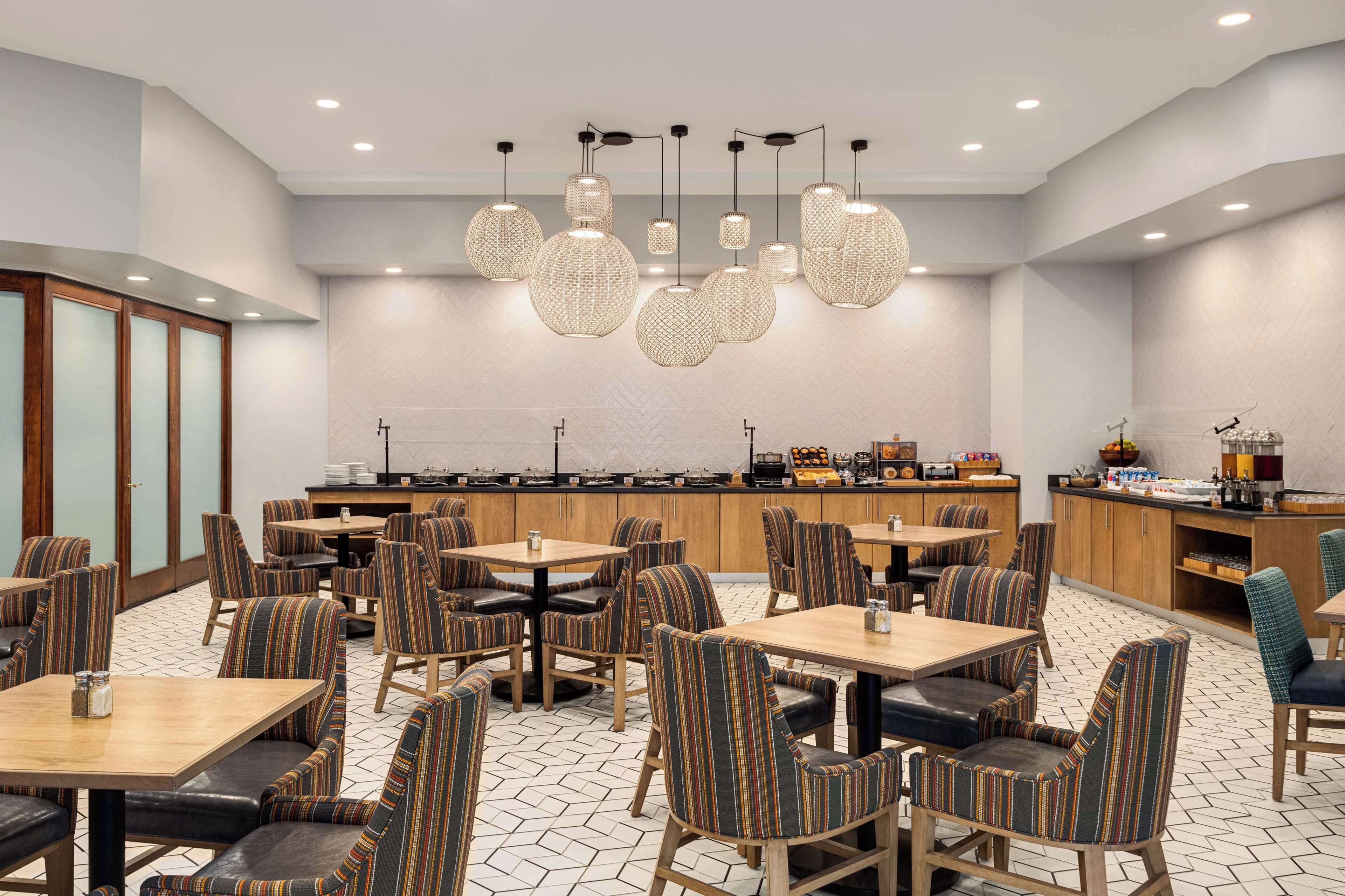Un comedor de hotel con sillas a rayas, mesas redondas y una barra central.