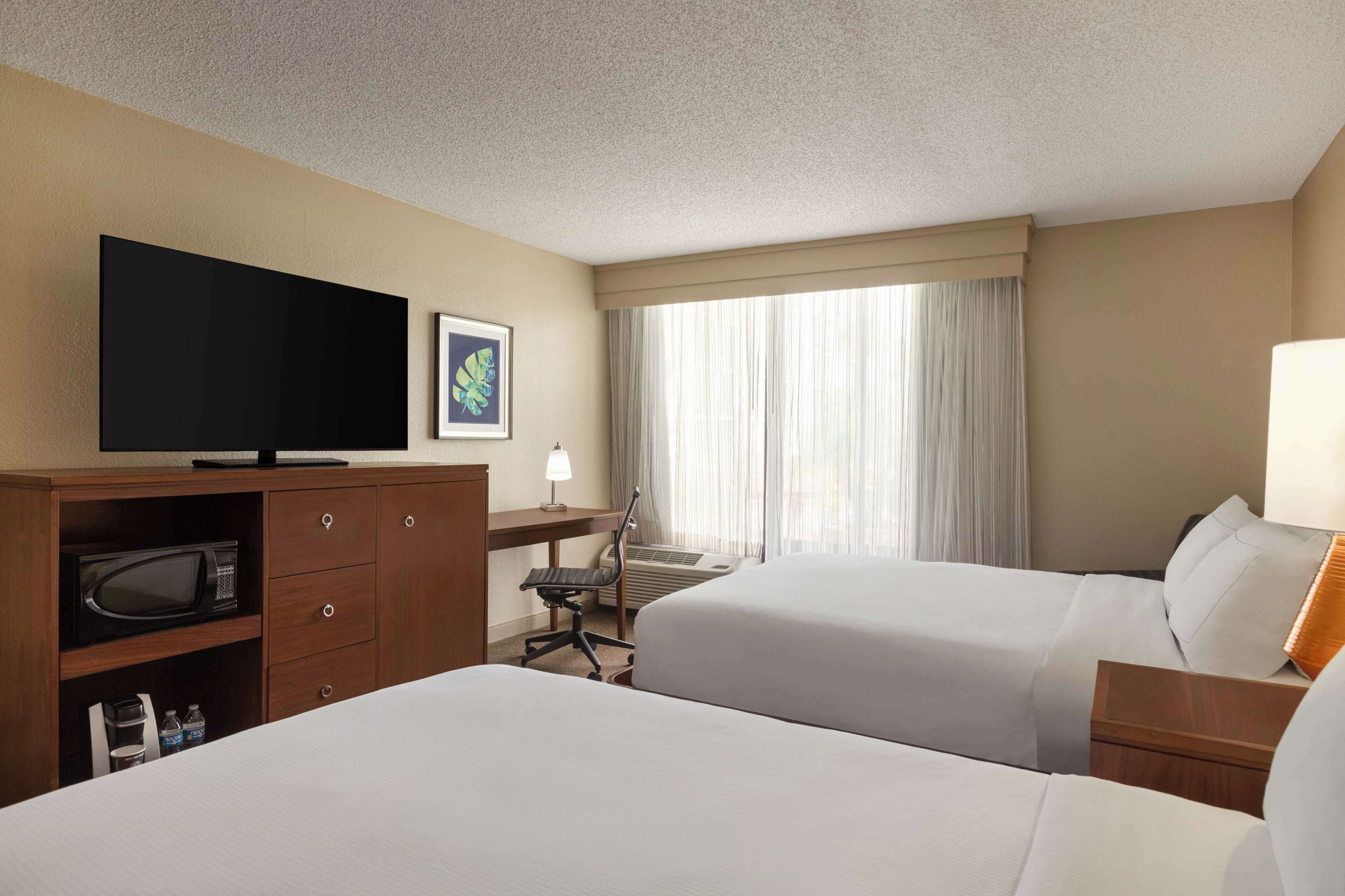 A hotel room with two beds, a desk, a television, and a window with curtains.