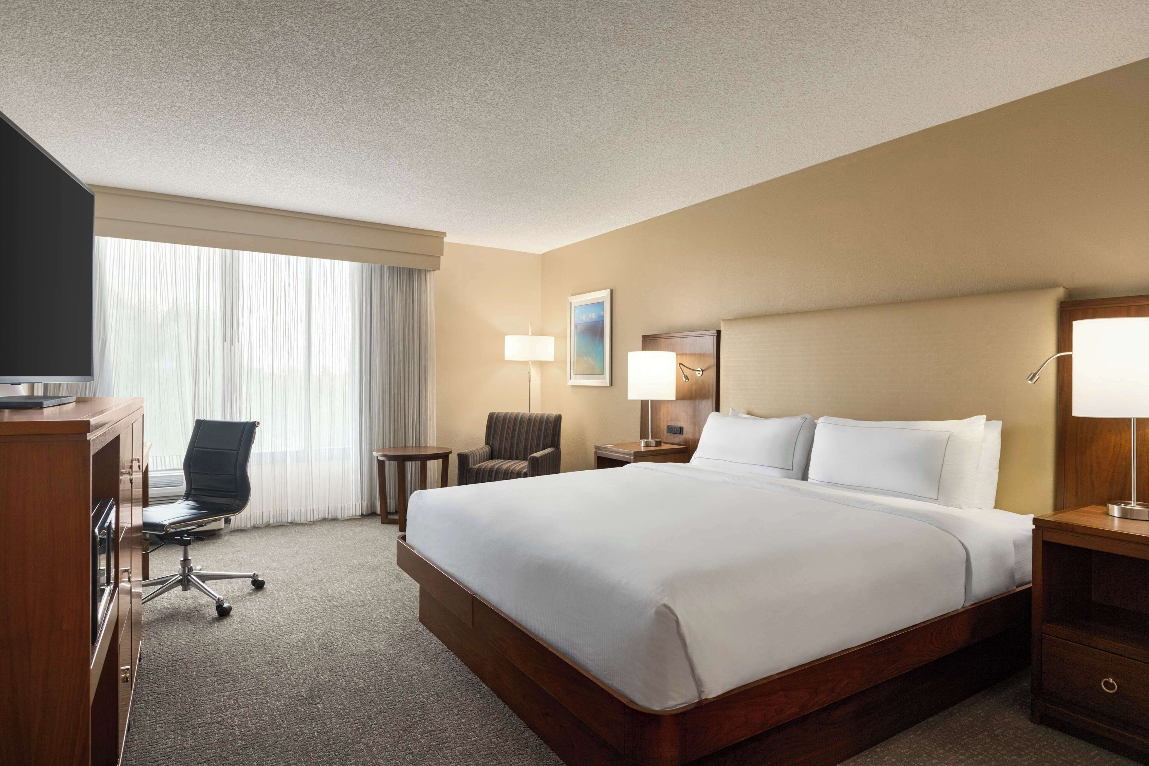 A hotel room with a large bed, a desk, a chair, a lamp, and a television.