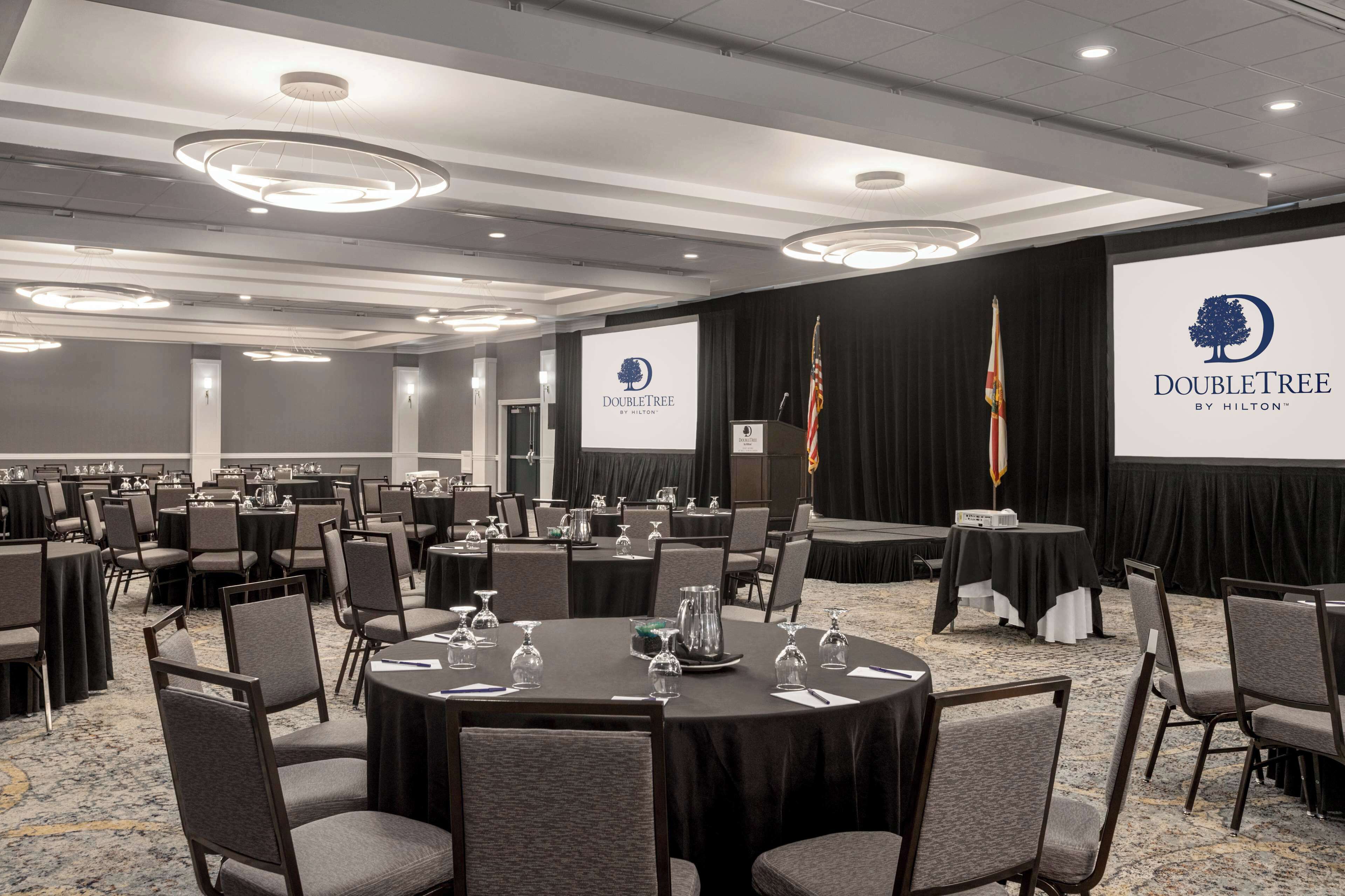 A conference room with round tables, chairs, and a stage with a podium.