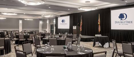 A conference room with round tables, chairs, and a stage with a podium.