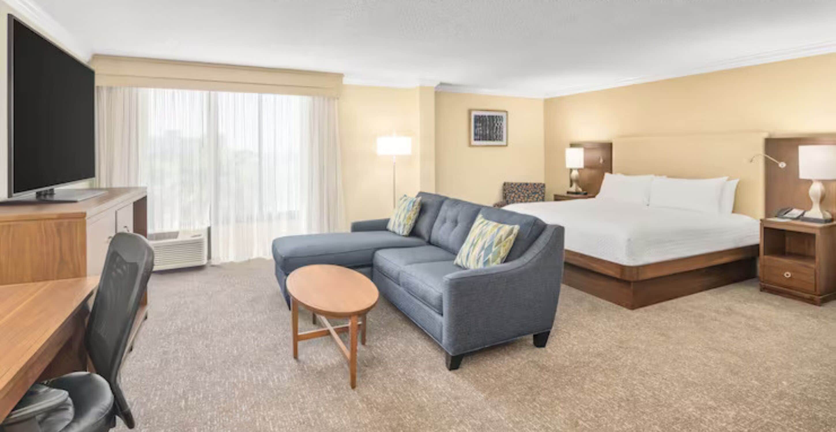 Ein Hotelzimmer mit Bett, Sofa, Schreibtisch, Fernseher und Lampe.