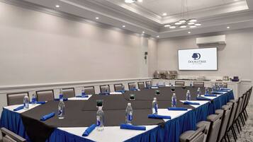 Un salón de conferencias con una larga mesa, sillas, botellas de agua y una pantalla que muestra el logotipo de DoubleTree.