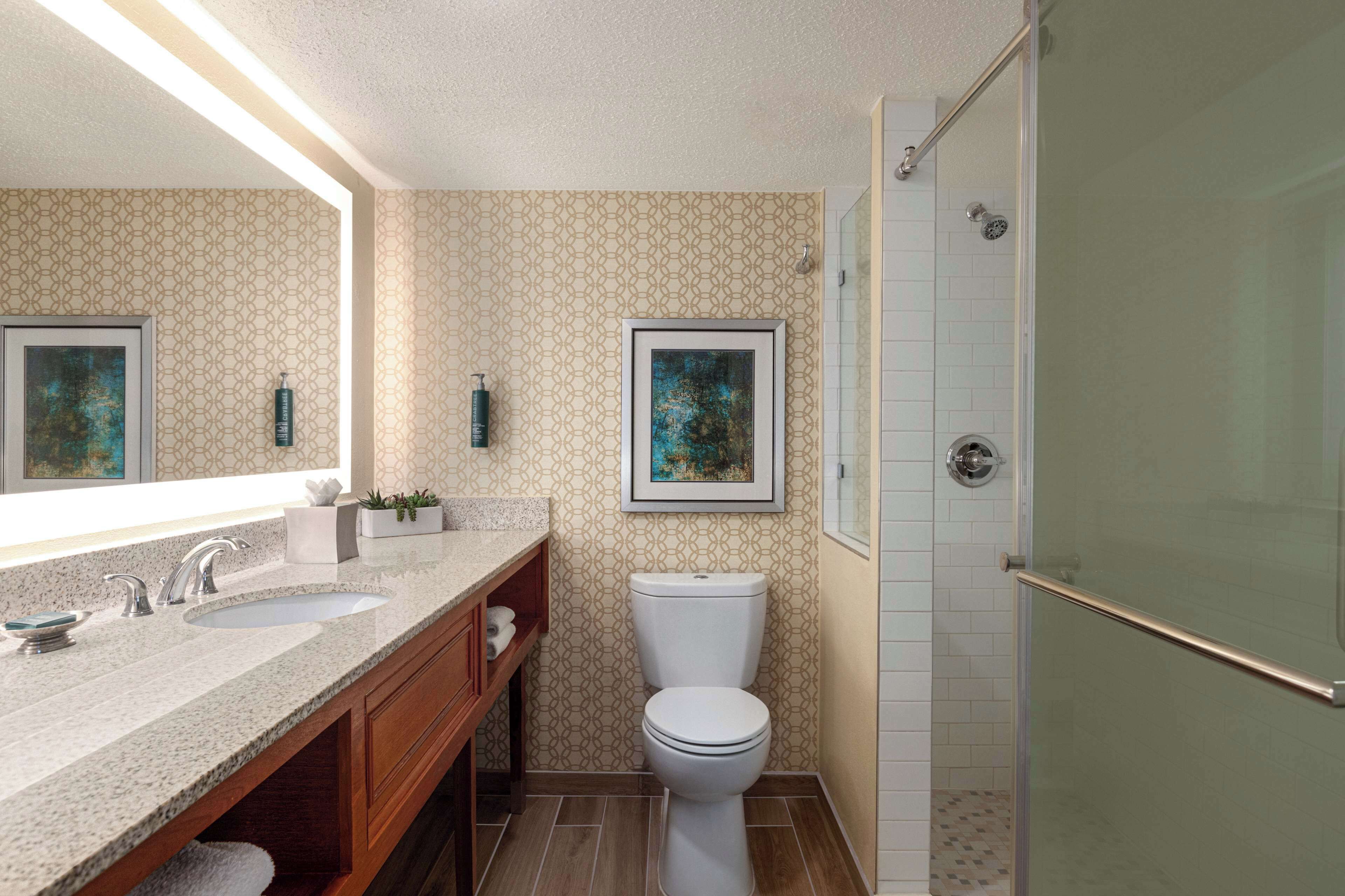 Un baño moderno con encimera de granito, dos lavamanos, inodoro y ducha con mampara de vidrio.