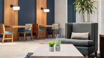 Un salon moderne avec un canapé gris, deux fauteuils en bois, une table à manger et deux lampes fixées au mur.