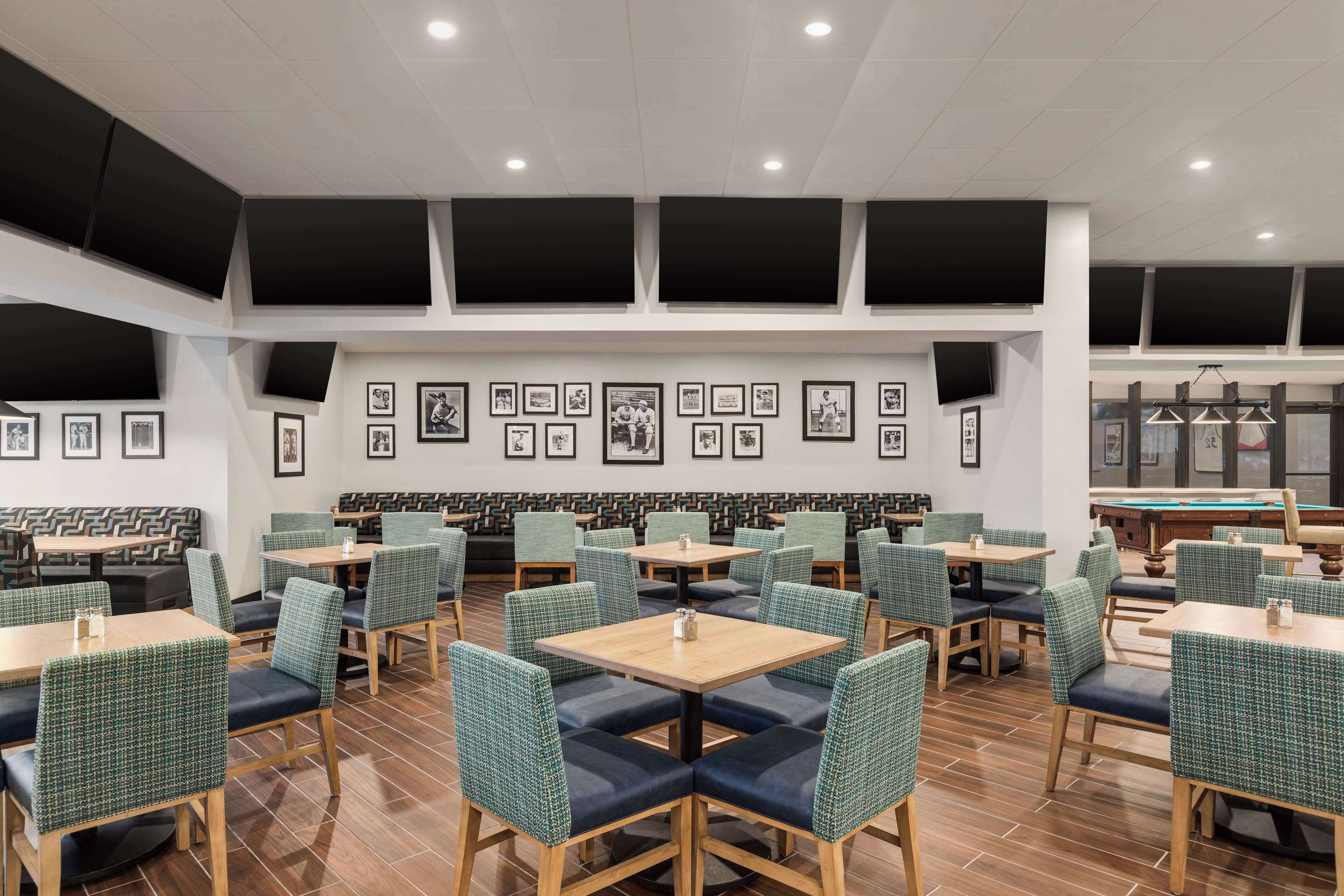 A restaurant with multiple tables and booths, framed pictures on the walls, and a pool table in the background.