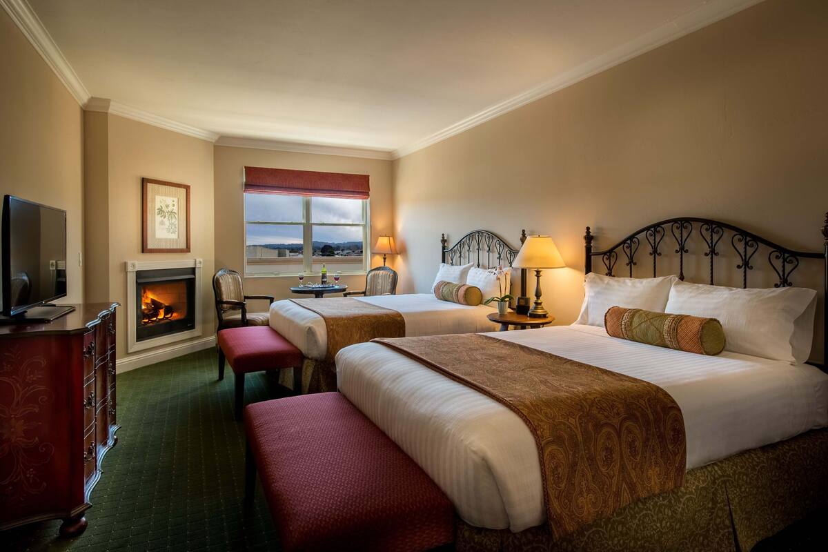 A hotel room with two beds, a fireplace, a television, and a view of the outside.