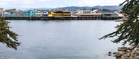 A waterfront area with buildings extending over the water, a dock, and a mountainous background.