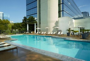 A swimming pool with lounge chairs and umbrellas, surrounded by a building with large windows and a modern design.