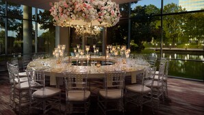 A round dining table with clear chairs, candles, and a floral centerpiece.
