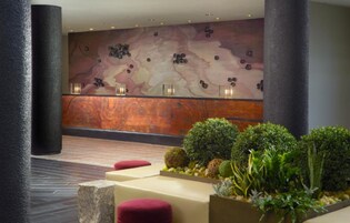 Un vestíbulo con un mostrador de recepción de mármol, asientos acolchados rojos y un gran mural abstracto en la pared.