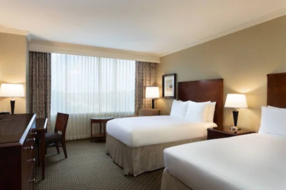 A hotel room with two beds, a desk, and a chair.
