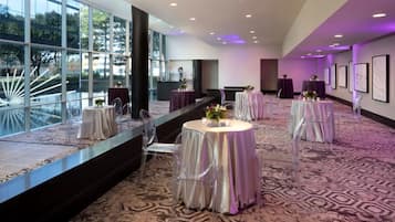 A spacious hall with round tables and chairs, large windows, and framed artwork on the walls.