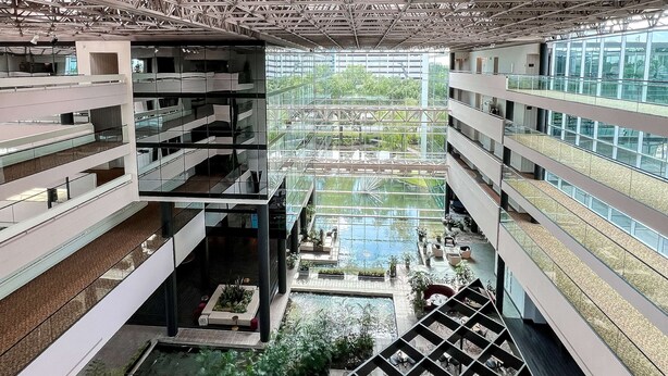 A multi-level atrium with a central water feature, glass railings, and outdoor seating areas.