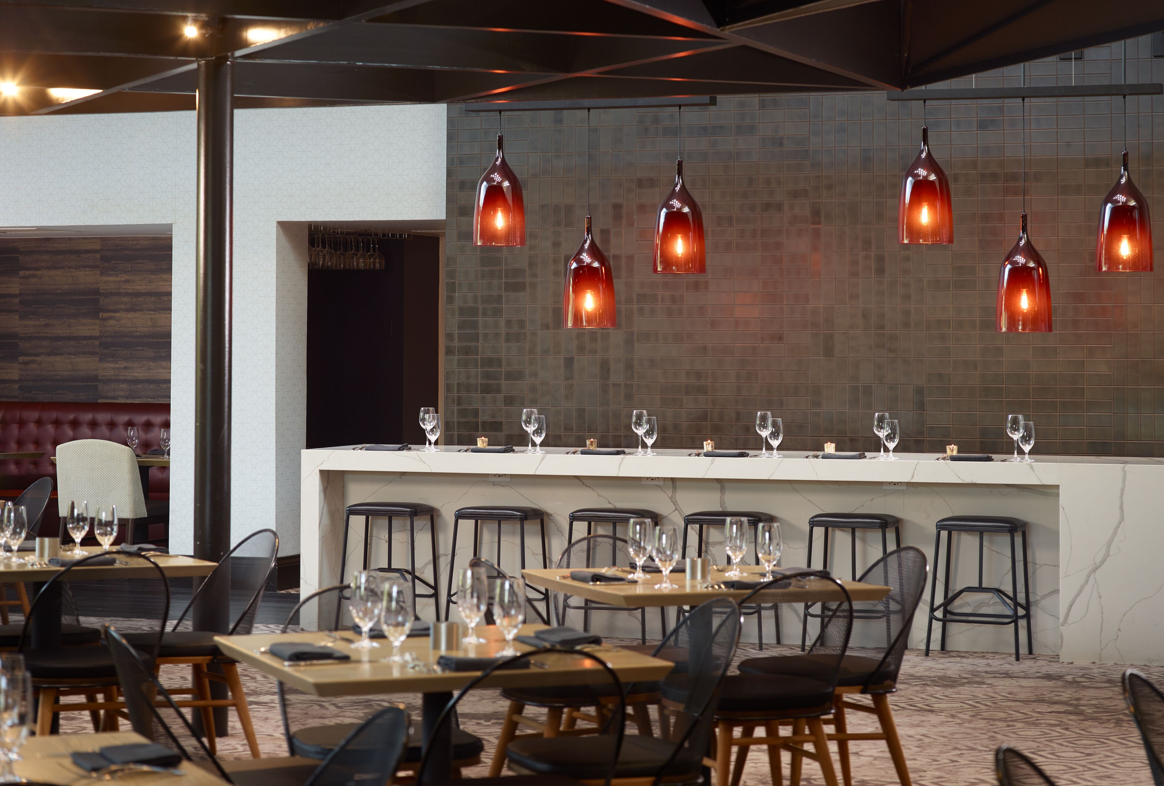A restaurant with a bar area, multiple tables with chairs, and hanging pendant lights.