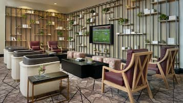 A modern lounge area with sofas, armchairs, and a coffee table. There is a television mounted on the wall displaying a sports game.