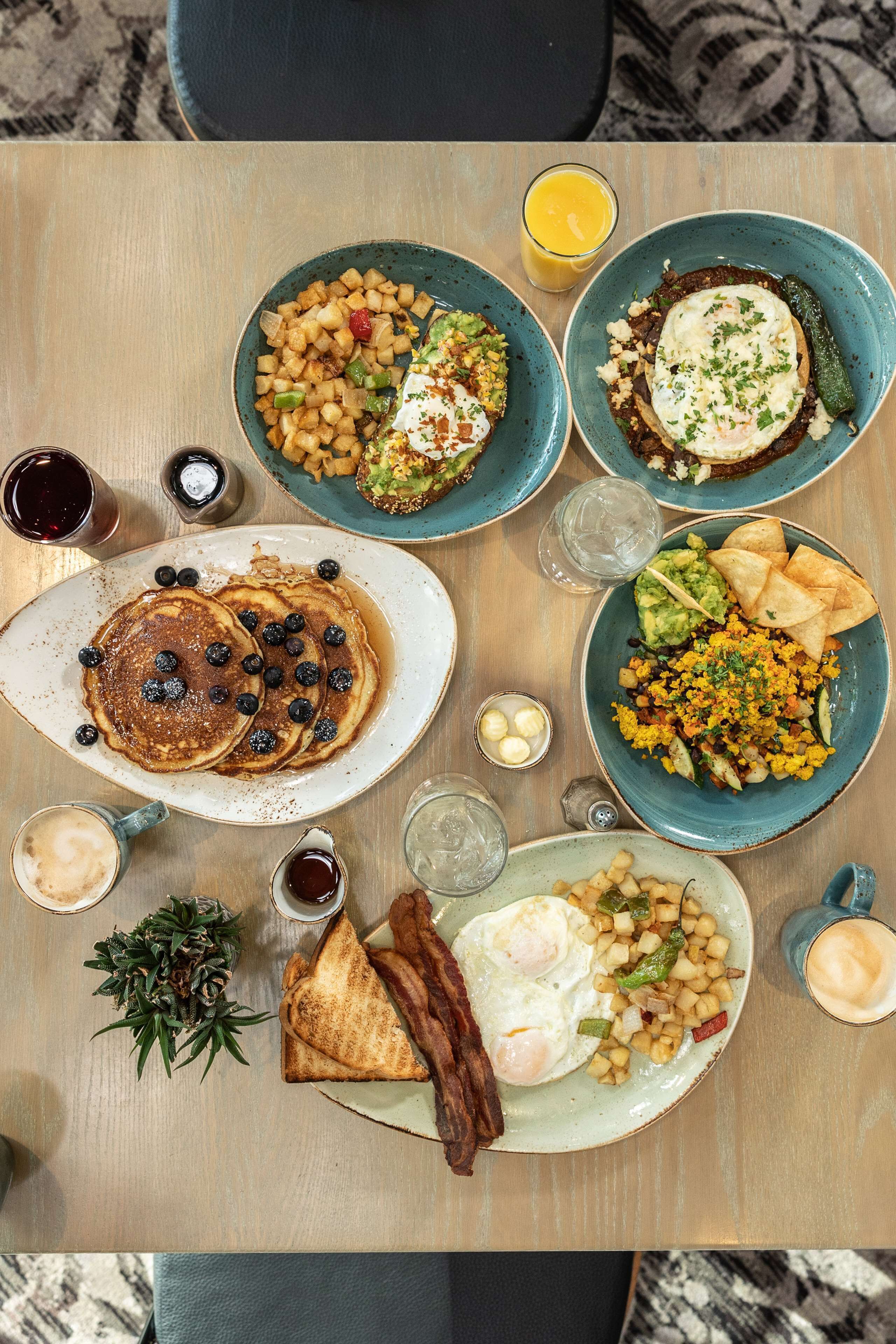 A breakfast table with pancakes, eggs, toast, and various side dishes.