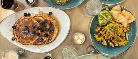 A breakfast table with pancakes, eggs, toast, and various side dishes.
