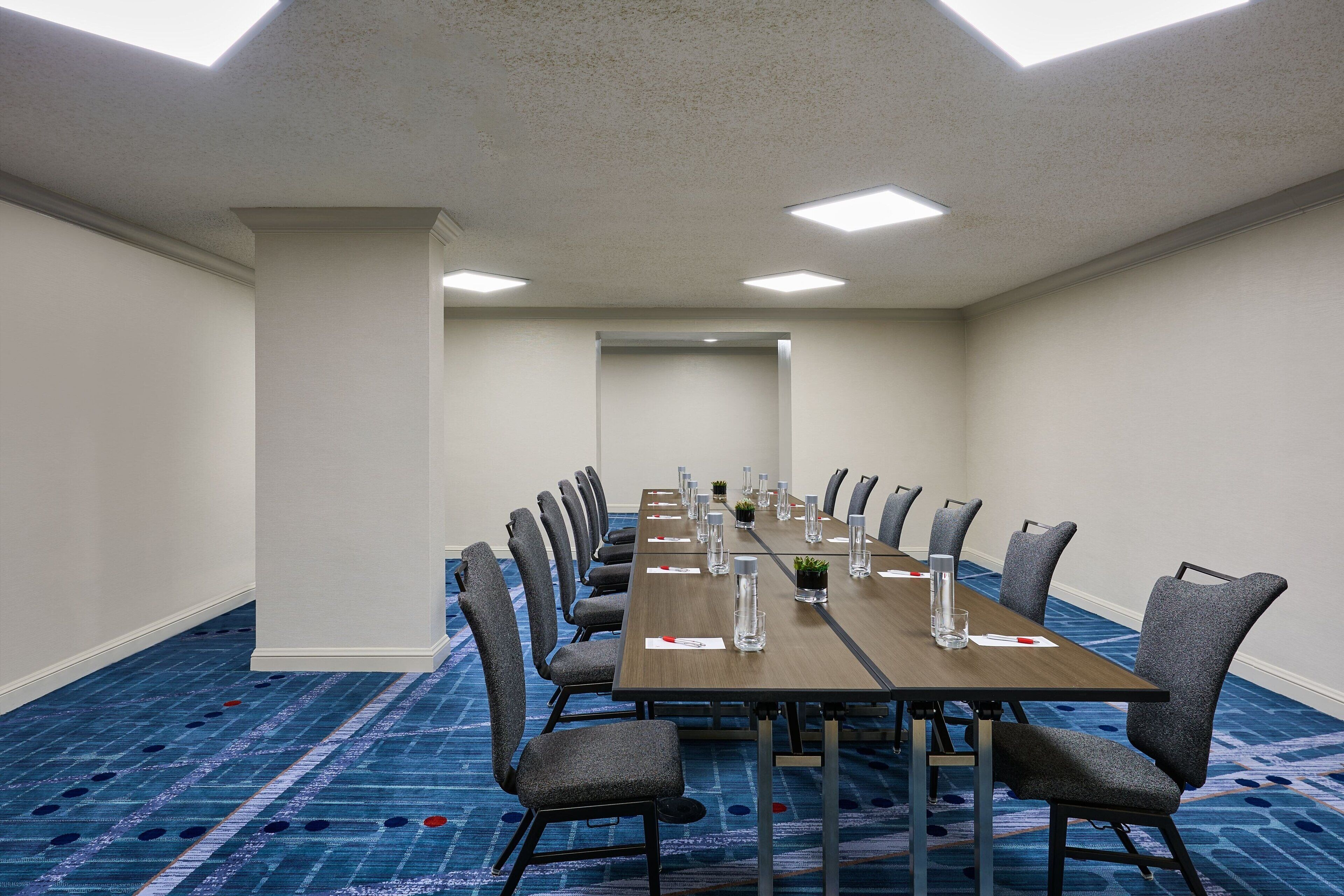 A conference room with a long table, chairs, and a carpeted floor.