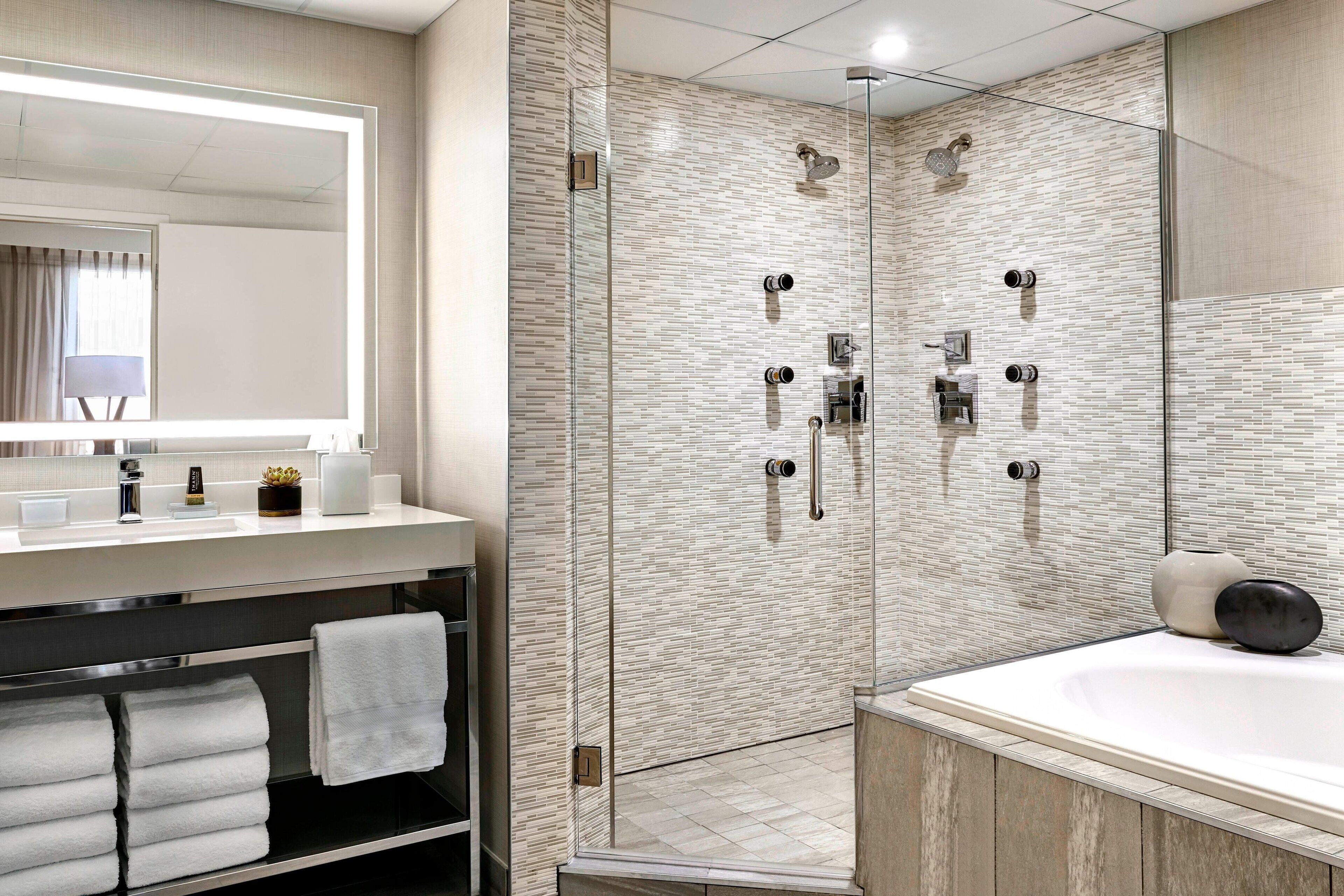 A modern bathroom with a glass-enclosed shower, a large mirror, and a white bathtub.