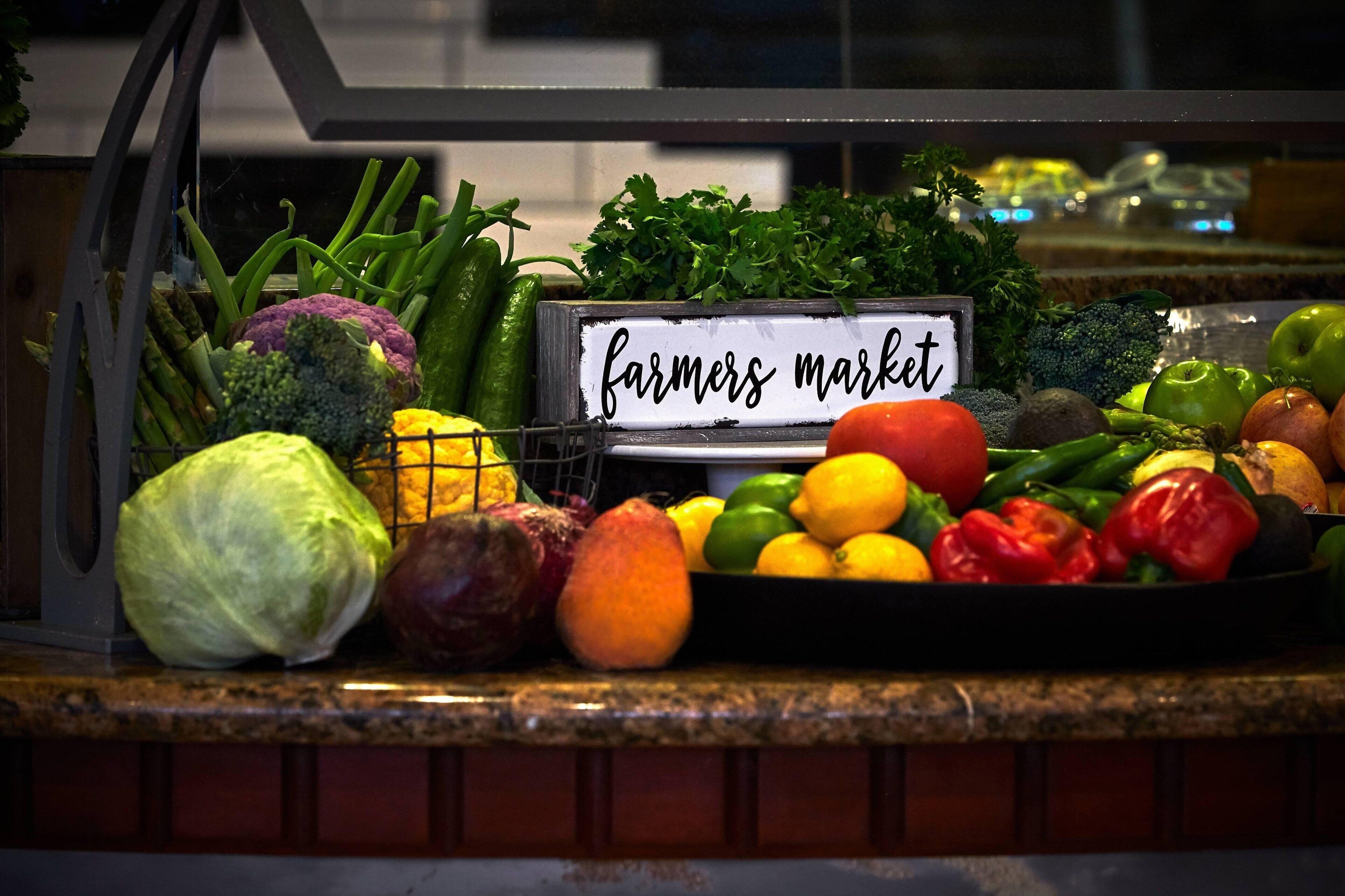 Variedad de verduras frescas exhibidas sobre una barra con un letrero que dice “farmers market”.