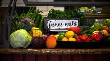 Variedad de verduras frescas exhibidas sobre una barra con un letrero que dice “farmers market”.