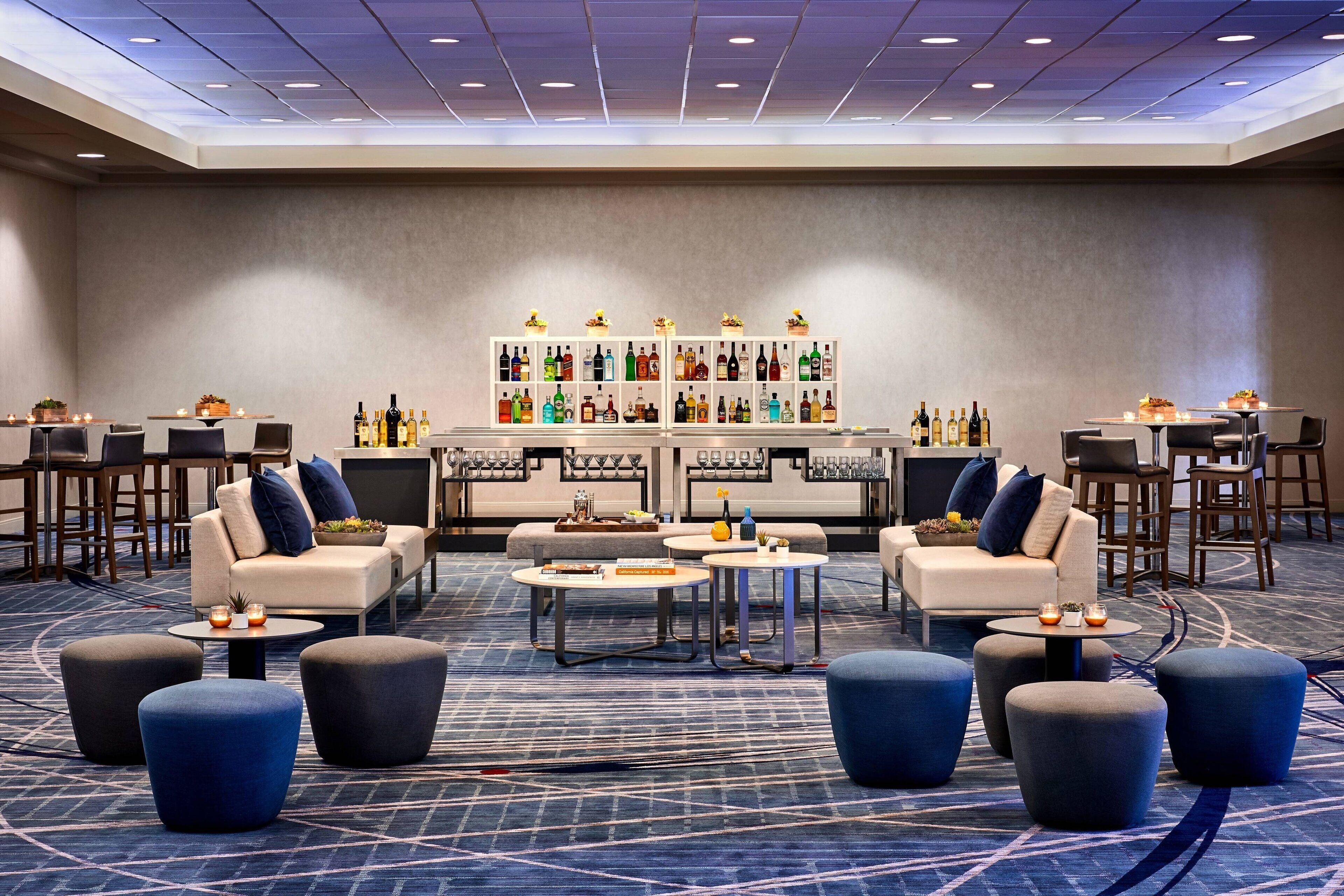 A modern lounge area with sofas, ottomans, and a bar with a variety of bottles.