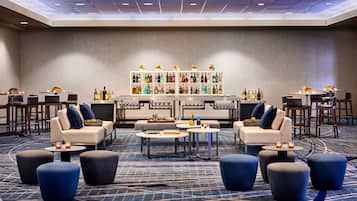 A modern lounge area with sofas, ottomans, and a bar with a variety of bottles.