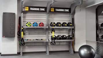 A gym with labeled 'TRAINING ZONE' signs, weight plates, and exercise equipment.