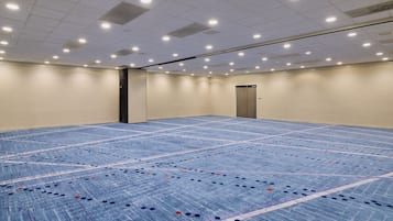 Une grande salle de conférence vide, dotée d’un tapis bleu et de murs blancs.