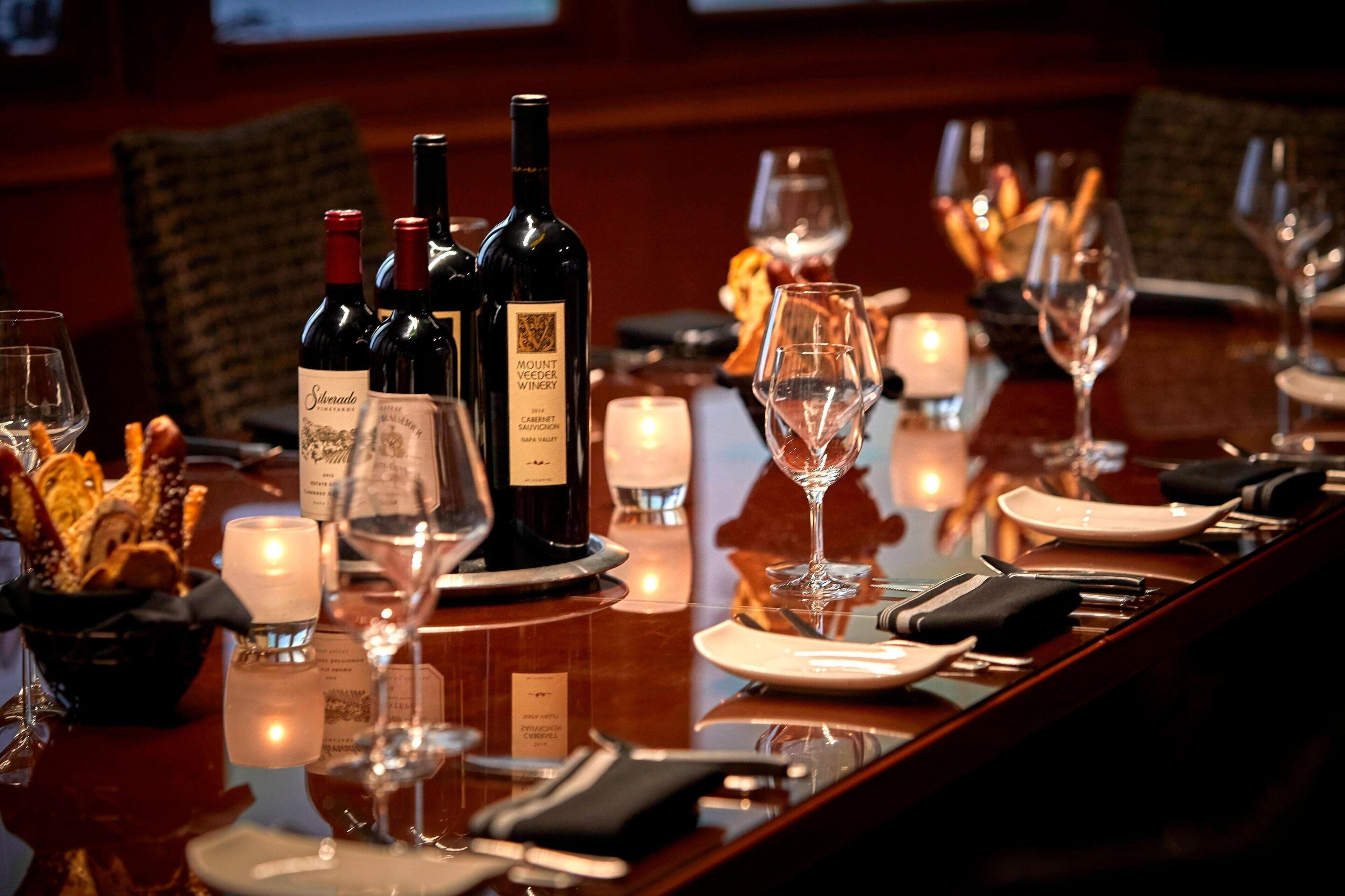 Una mesa de comedor elegantemente dispuesta con botellas de vino, copas y velas.