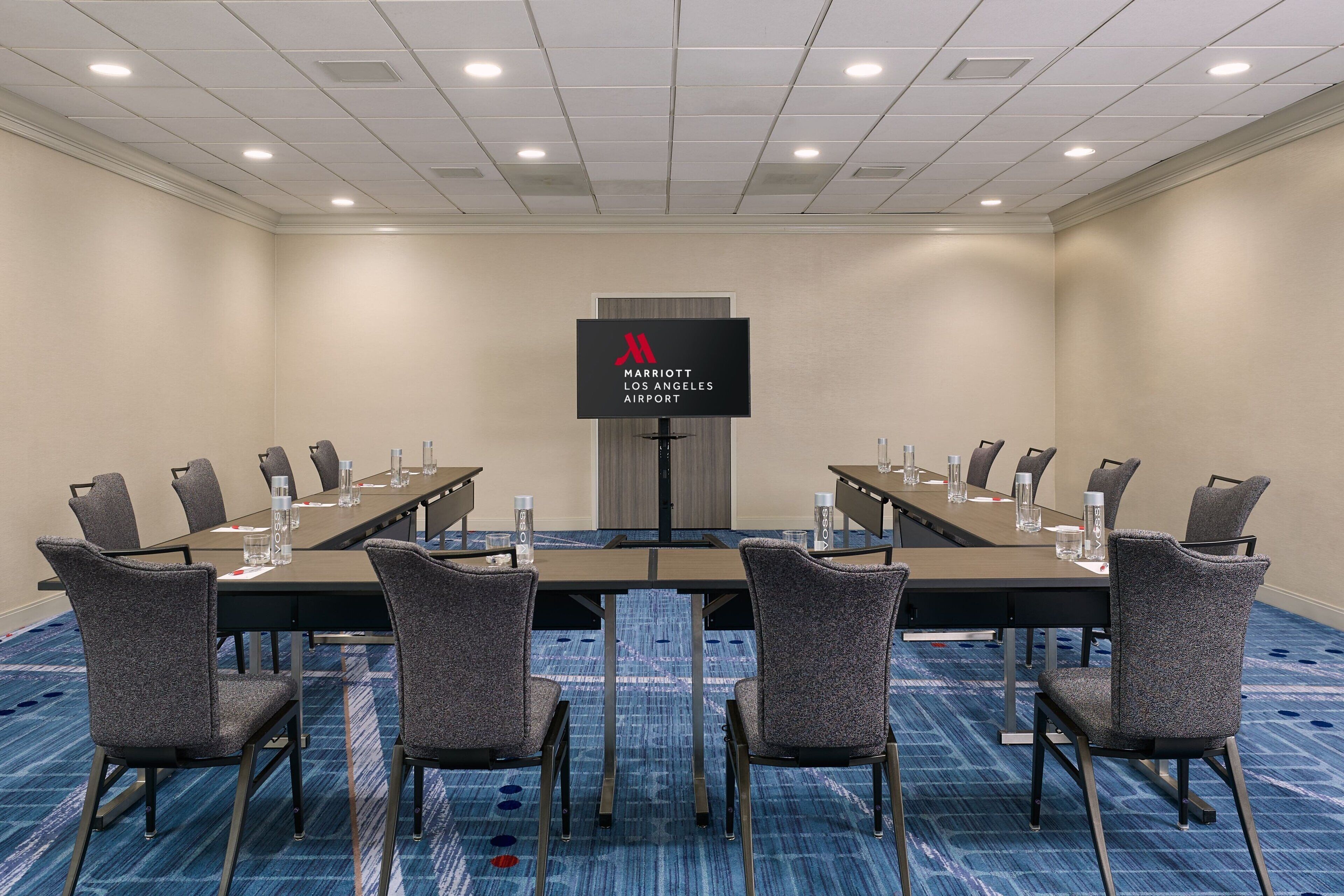 A conference room with a long table, chairs, a screen, and a carpeted floor.