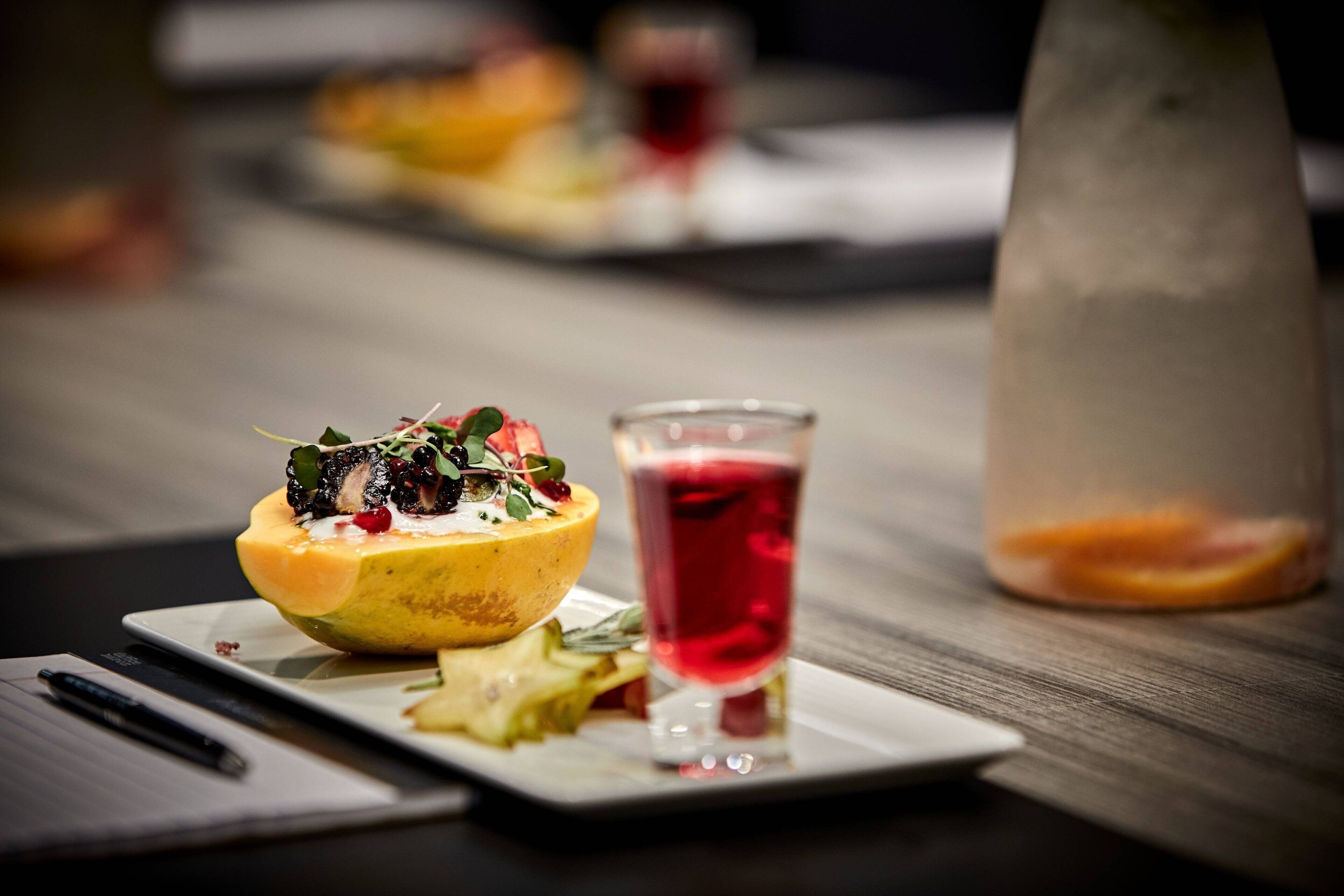 Una mesa de comedor con un plato de comida, un vaso de bebida roja y una botella de agua.
