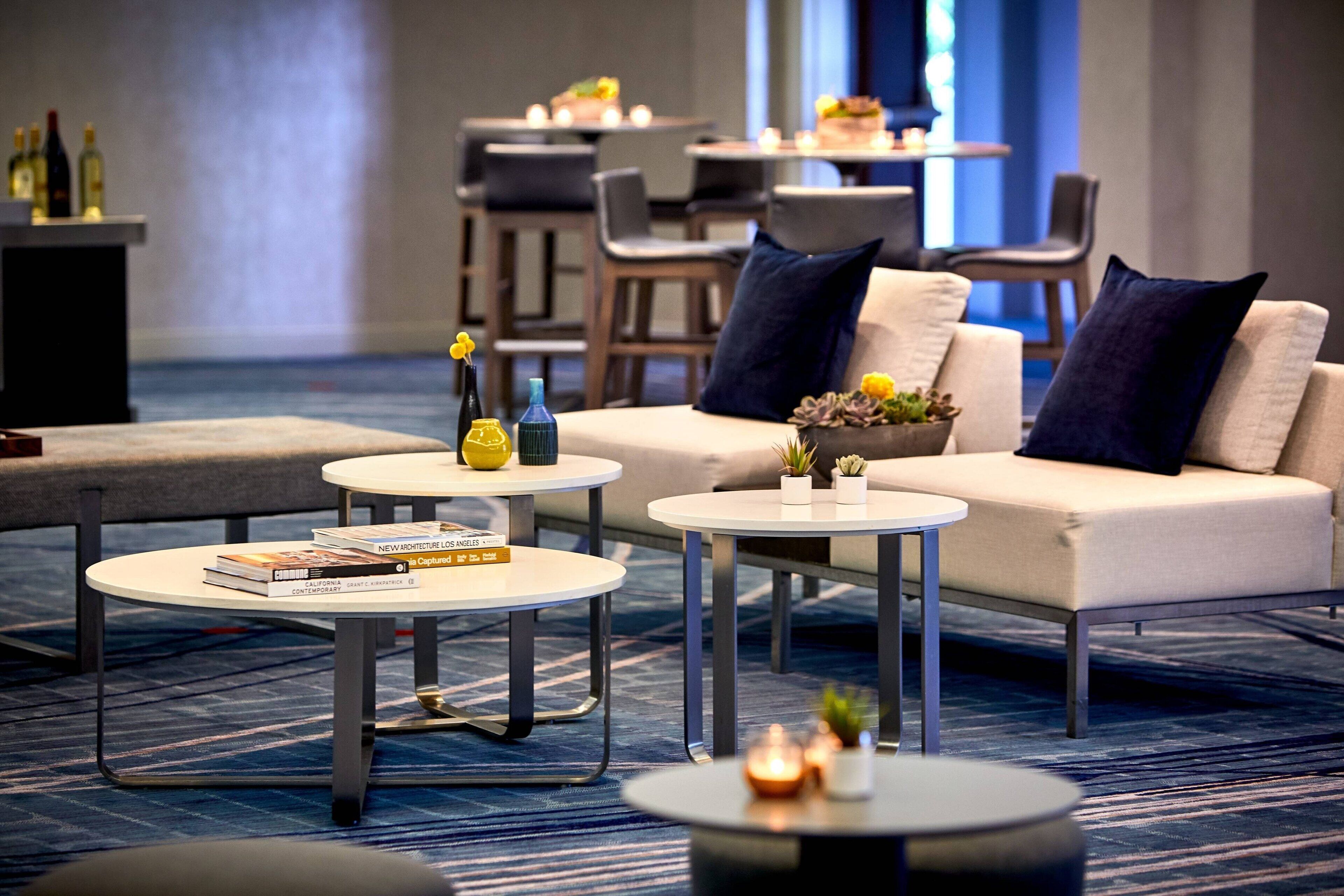 Eine moderne Hotelhalle mit einer Couch, zwei Couchtischen und einem kleinen Tisch mit Büchern und Kerzen.