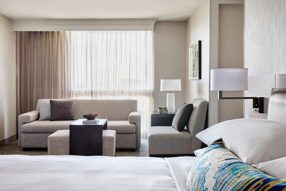 Ein Hotelzimmer mit einem Bett, einem Sofa, einem Sessel, einem kleinen Tisch und einer Lampe.