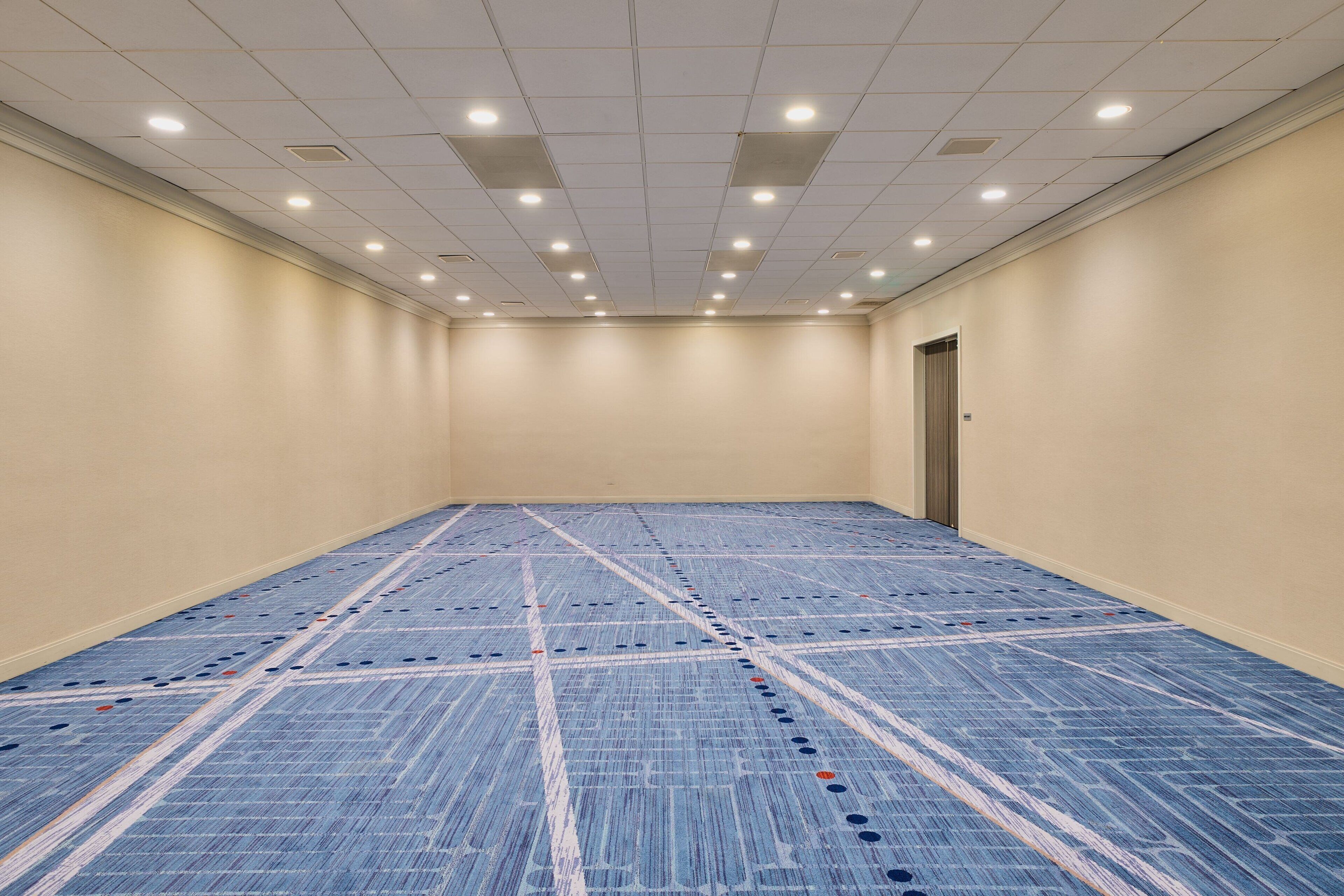 Habitación de hotel con un amplio suelo alfombrado, una puerta e iluminación empotrada en el techo.