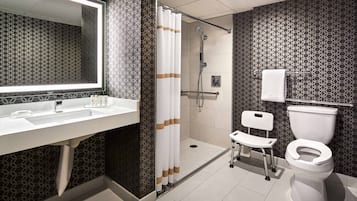 A modern bathroom with a large mirror, a shower, a toilet, and a sink.
