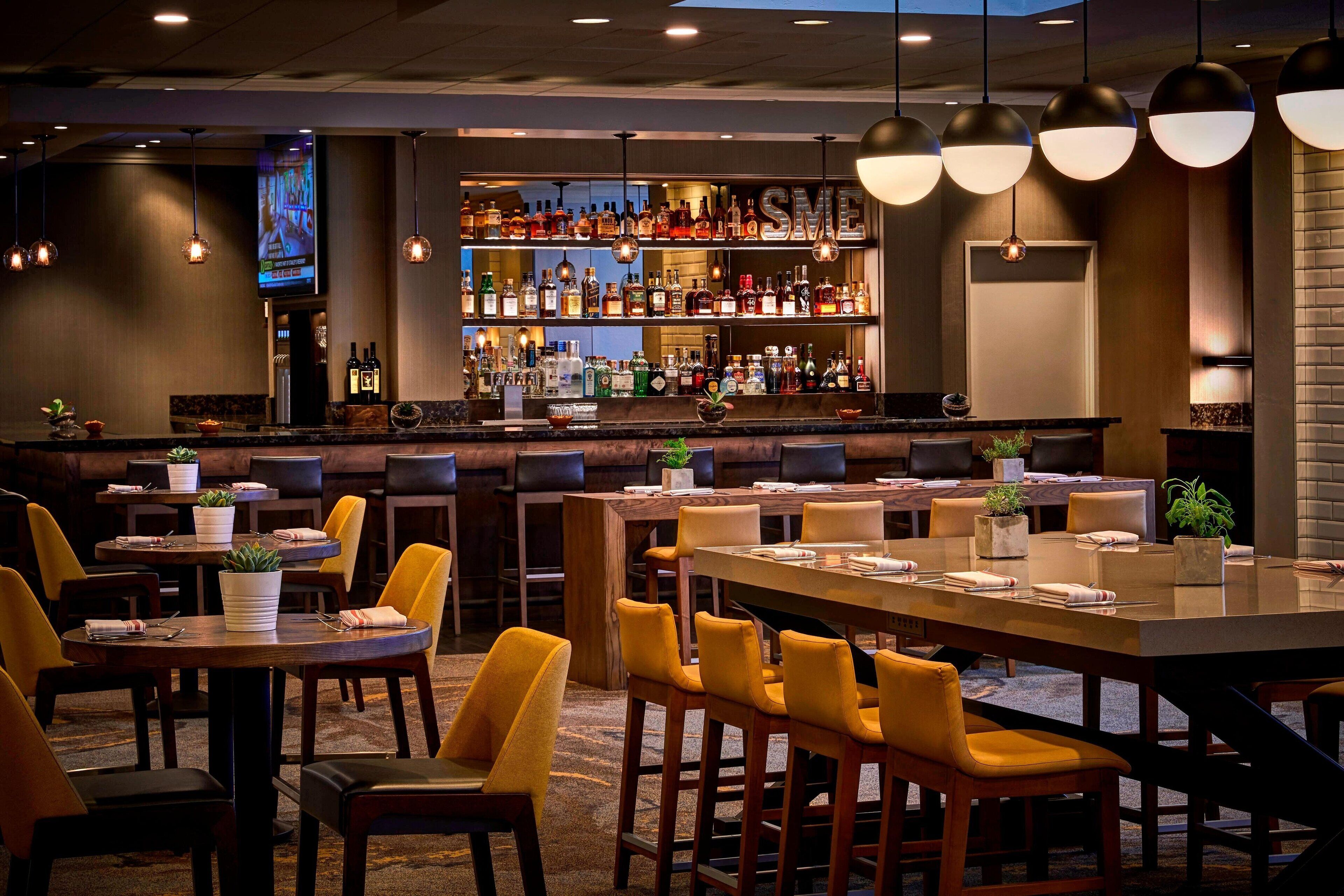 A bar area with multiple seating options, including bar stools and tables, and a well-stocked liquor shelf.