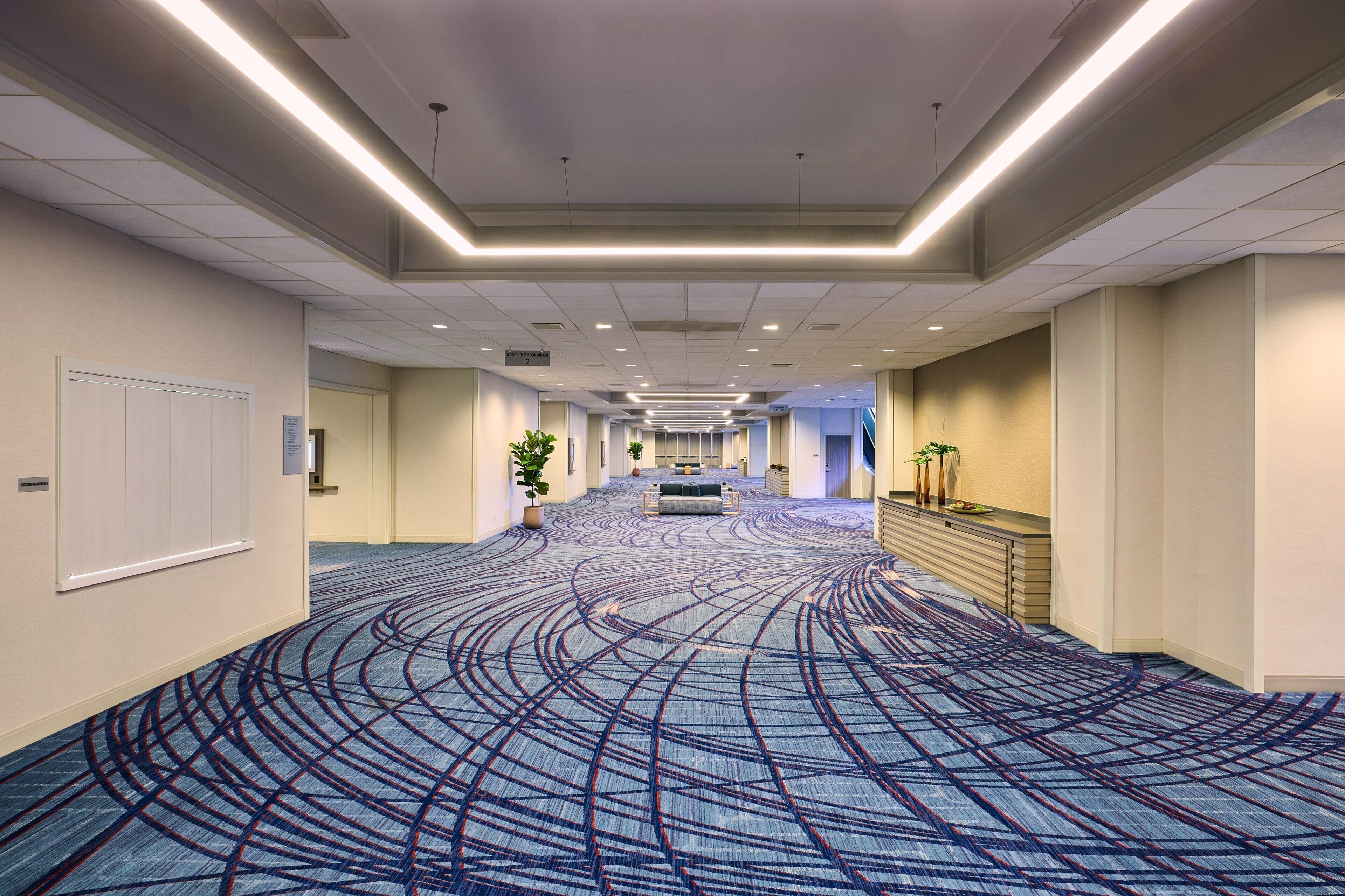 A spacious hotel corridor with a patterned carpet, a reception desk, and a seating area.