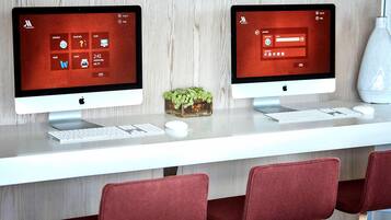 Two Apple iMac computers on a white desk with a keyboard, mouse, and a small plant.