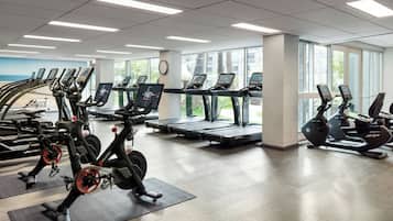 Een fitnessruimte met meerdere cardioapparaten, waaronder loopbanden en elliptische trainers, gerangschikt in rijen.