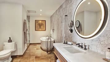 A modern bathroom with a marble vanity, a large mirror with a lighted frame, a bathtub, and a toilet.