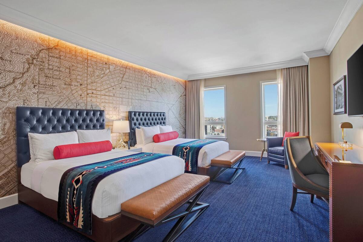 A hotel room with two beds, a desk, and a view of the city.