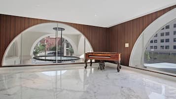 Un hallo espacioso con un piano de cola, una fuente y grandes ventanales de arco que ofrecen vistas panorámicas de la ciudad.