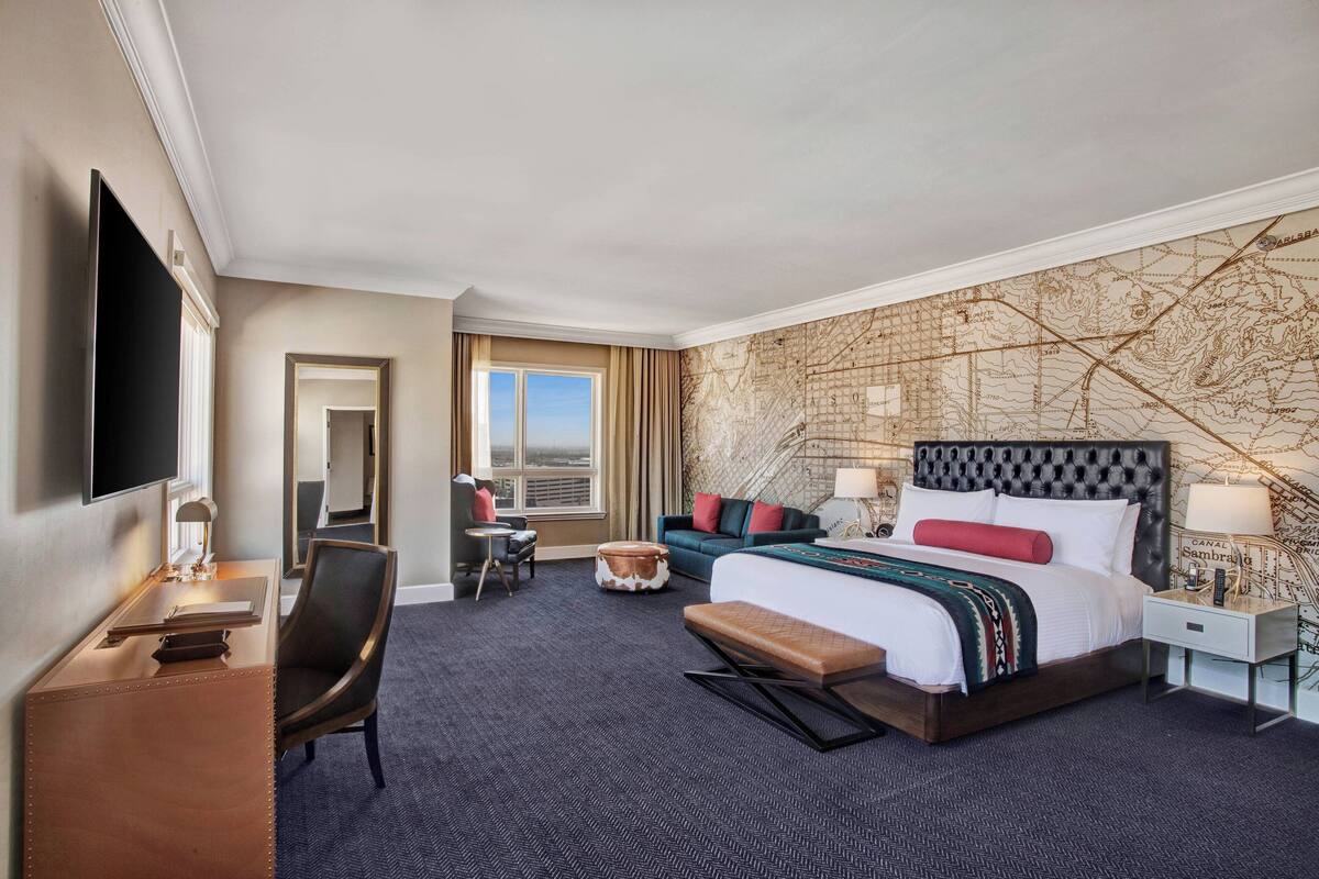 A hotel room with a large bed, a desk, a chair, a TV, and a map wall.