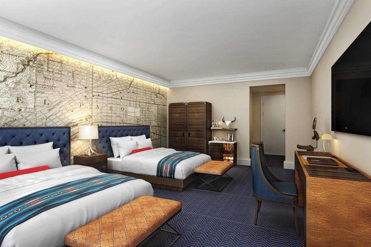 A hotel room with a large bed, two smaller beds, a desk, and a map on the wall.