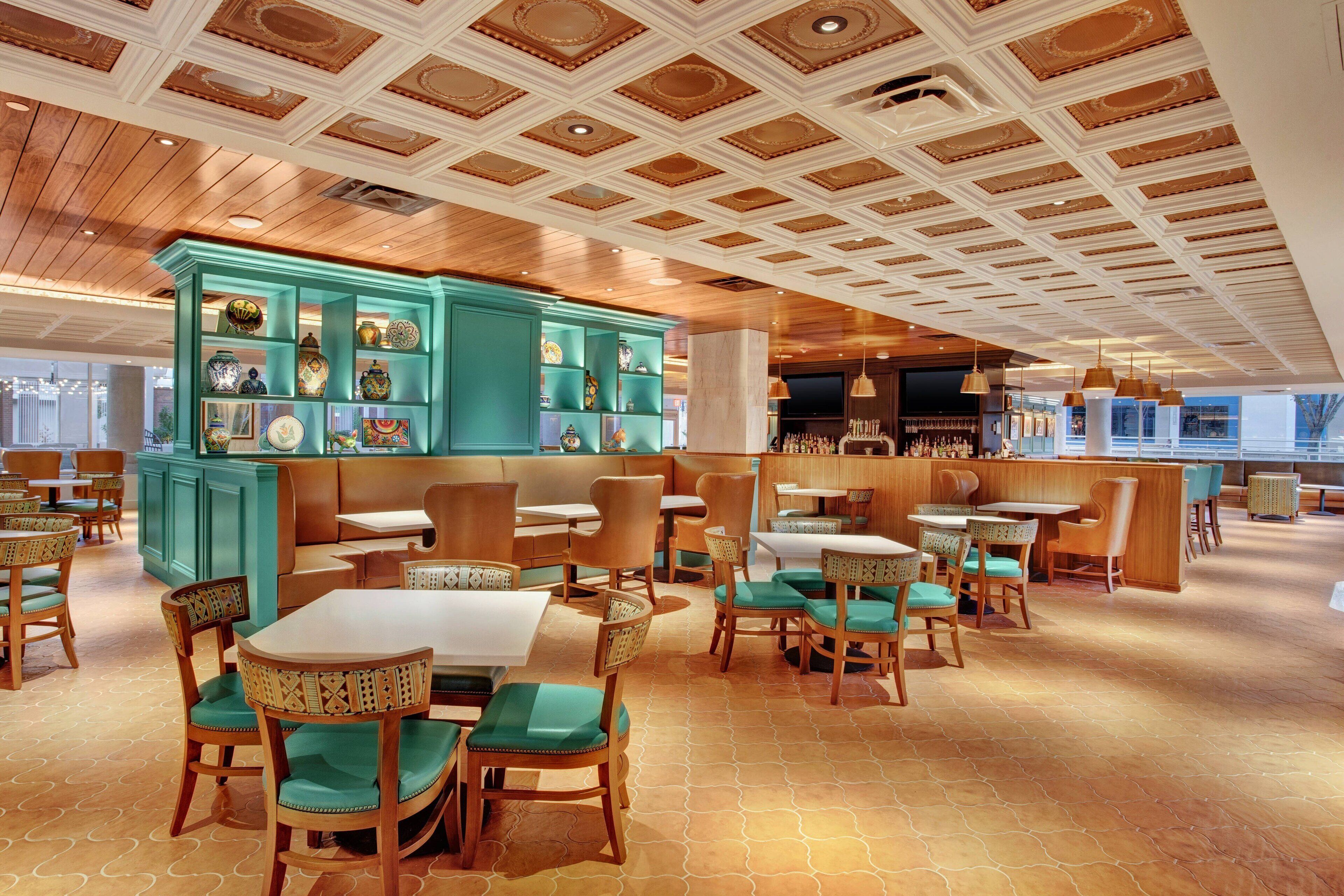 A restaurant with wooden tables and chairs, a teal-colored bar area, and a patterned ceiling.