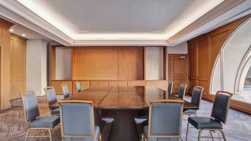 A conference room with a long table and 10 chairs, wooden paneling on the walls, and a large window on the right.