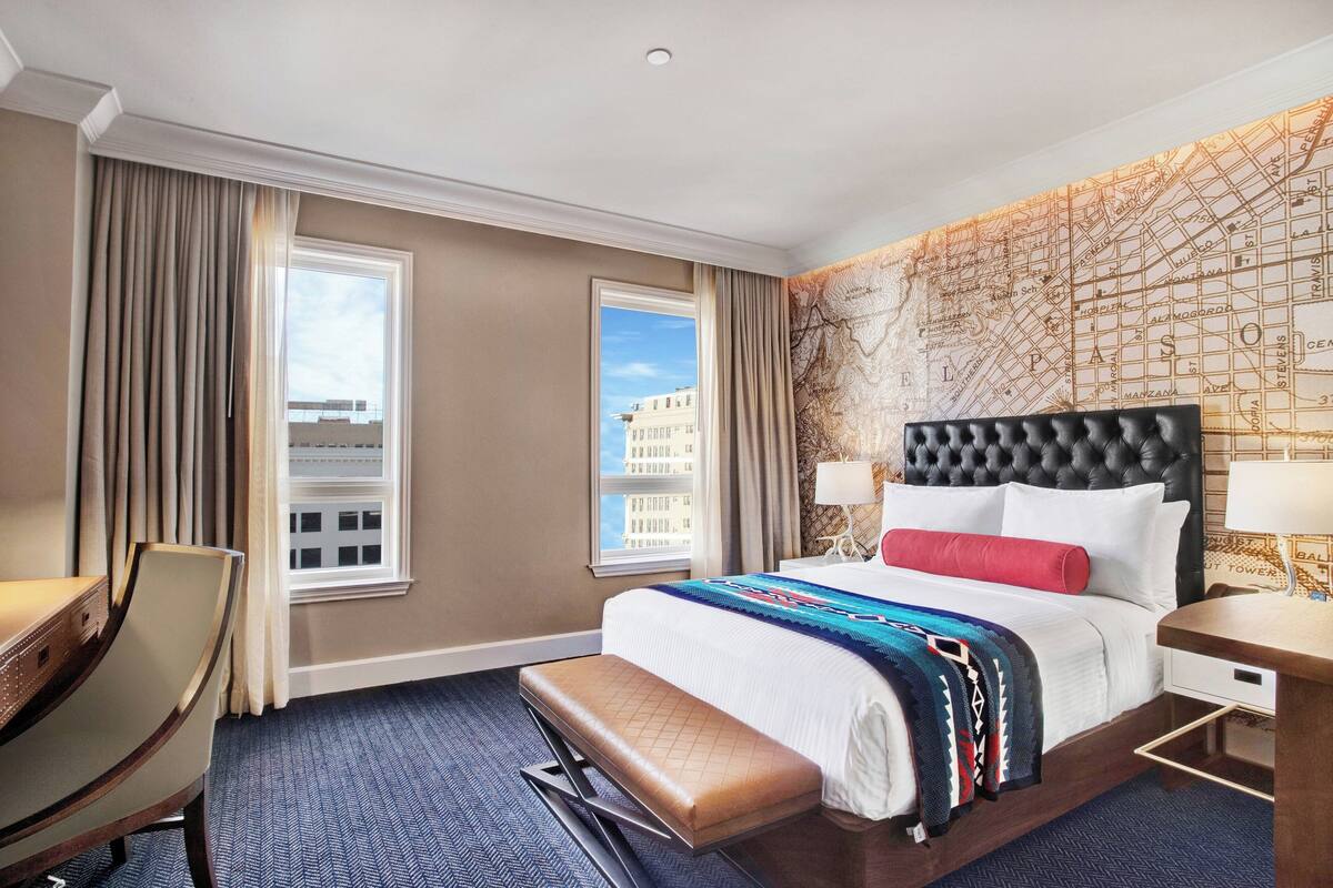 A hotel room with a large bed, a desk, a chair, and a window with curtains.