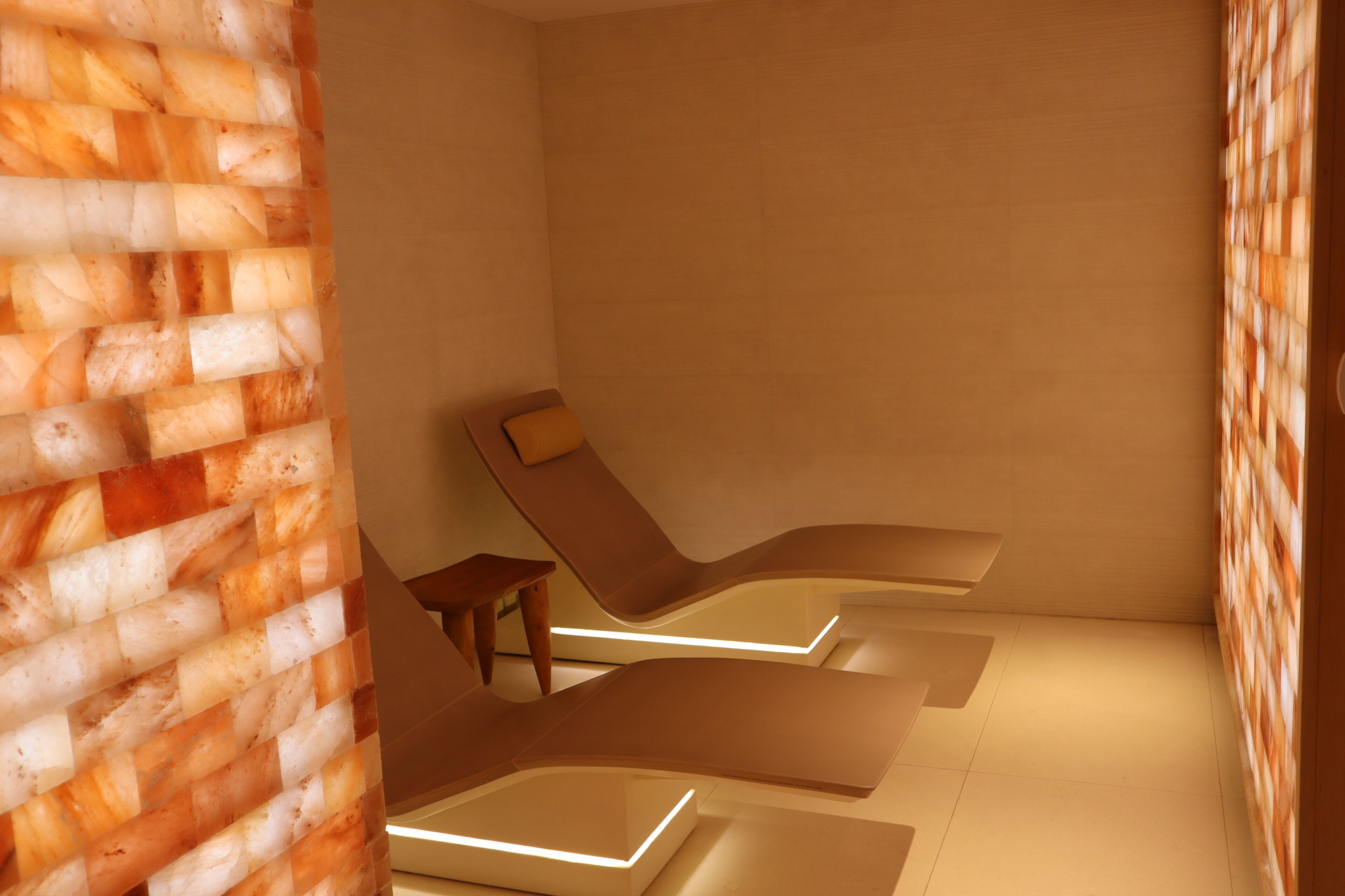 A spa room with two reclining chairs, a small wooden table, and a textured wall.